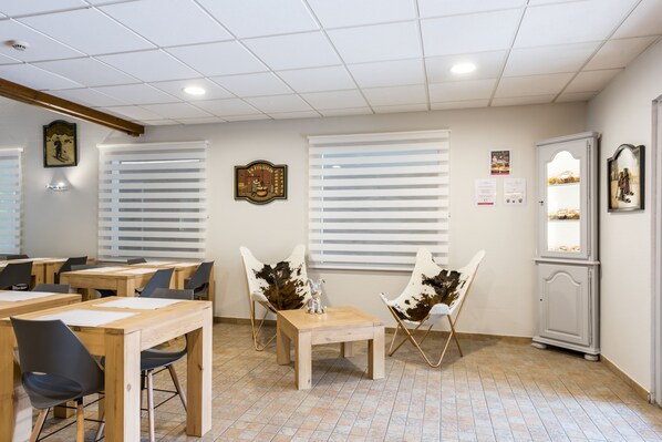 A room with wooden tables and chairs, a small table with decorative items, and a cabinet with glass doors. - Fasthôtel Thônes (Thones)