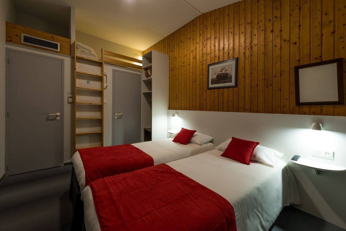A hotel room with two beds, wooden paneling on the walls, a wardrobe, and a shelf unit.