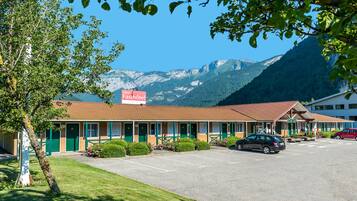 A motel with a mountain view, green doors, and a parking lot with cars.