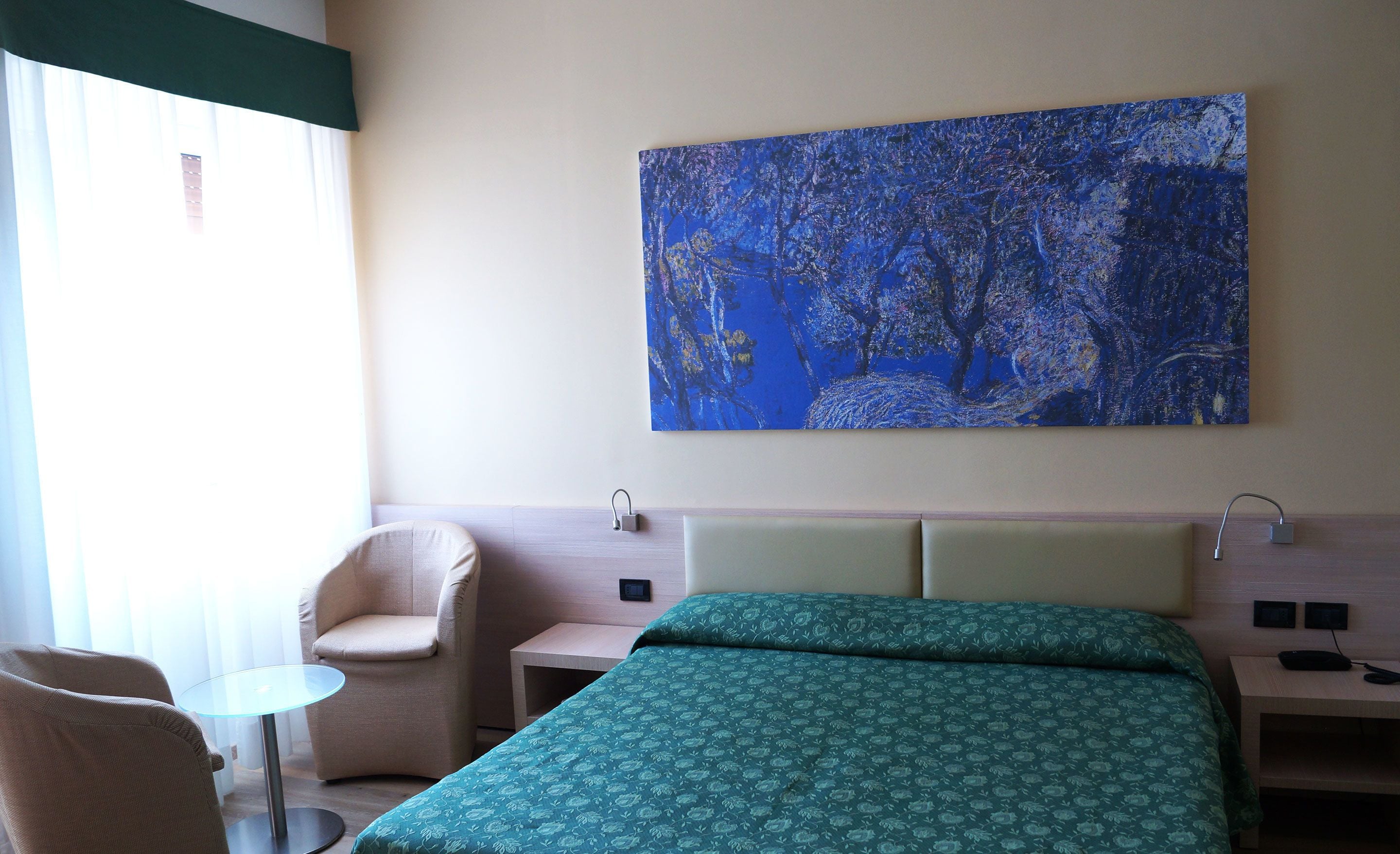 Een hotelkamer met een bed, een stoel, een tafeltje en een schilderij aan de muur.