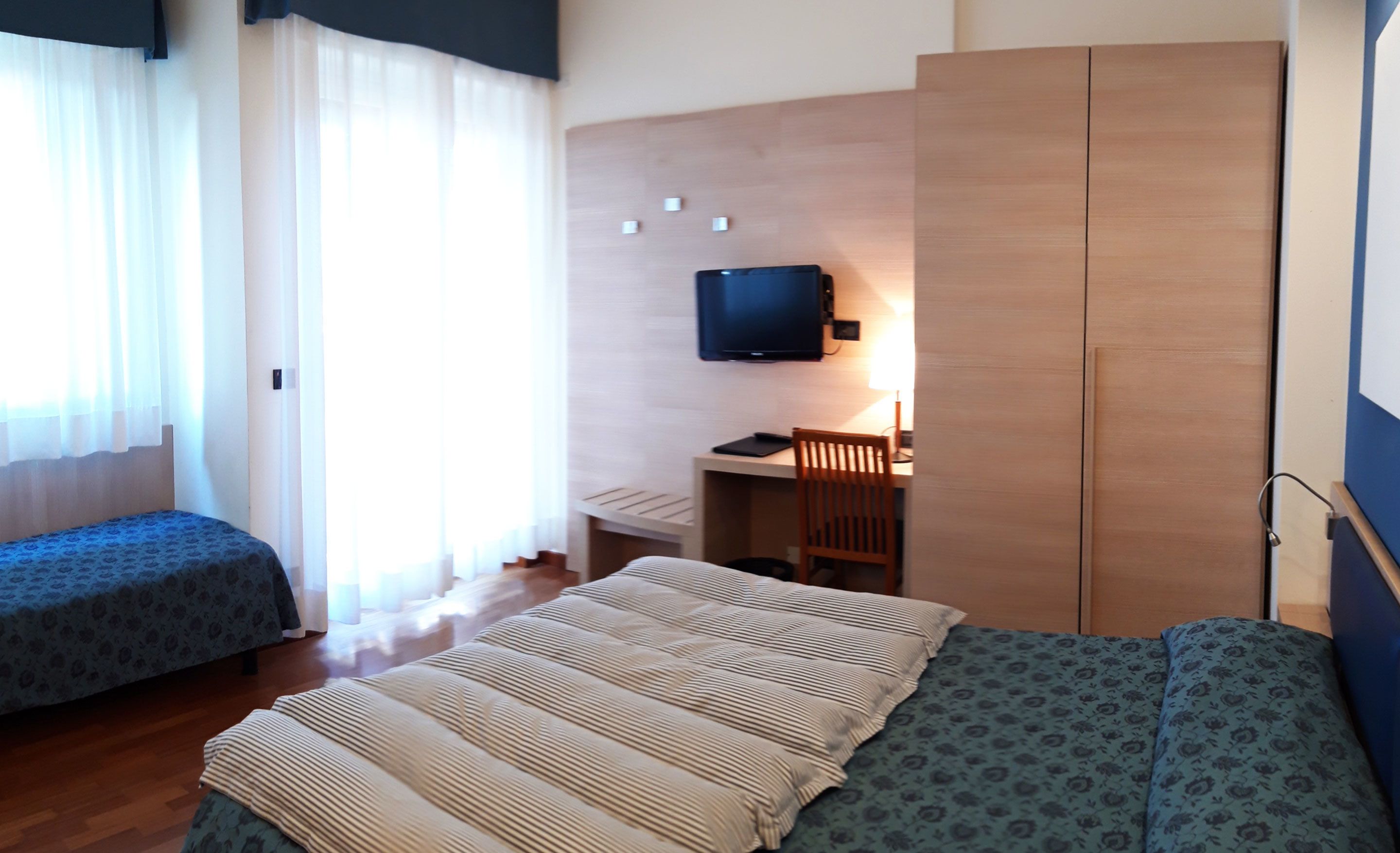 A hotel room with two beds, a desk with a chair, a television, and a wardrobe.