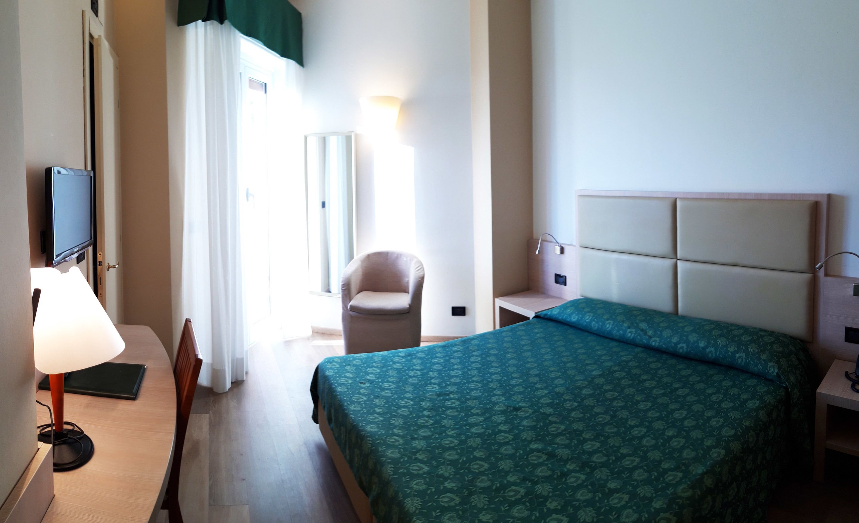 Una habitación de hotel con cama, una silla, un escritorio, un televisor y una ventana con cortinas.