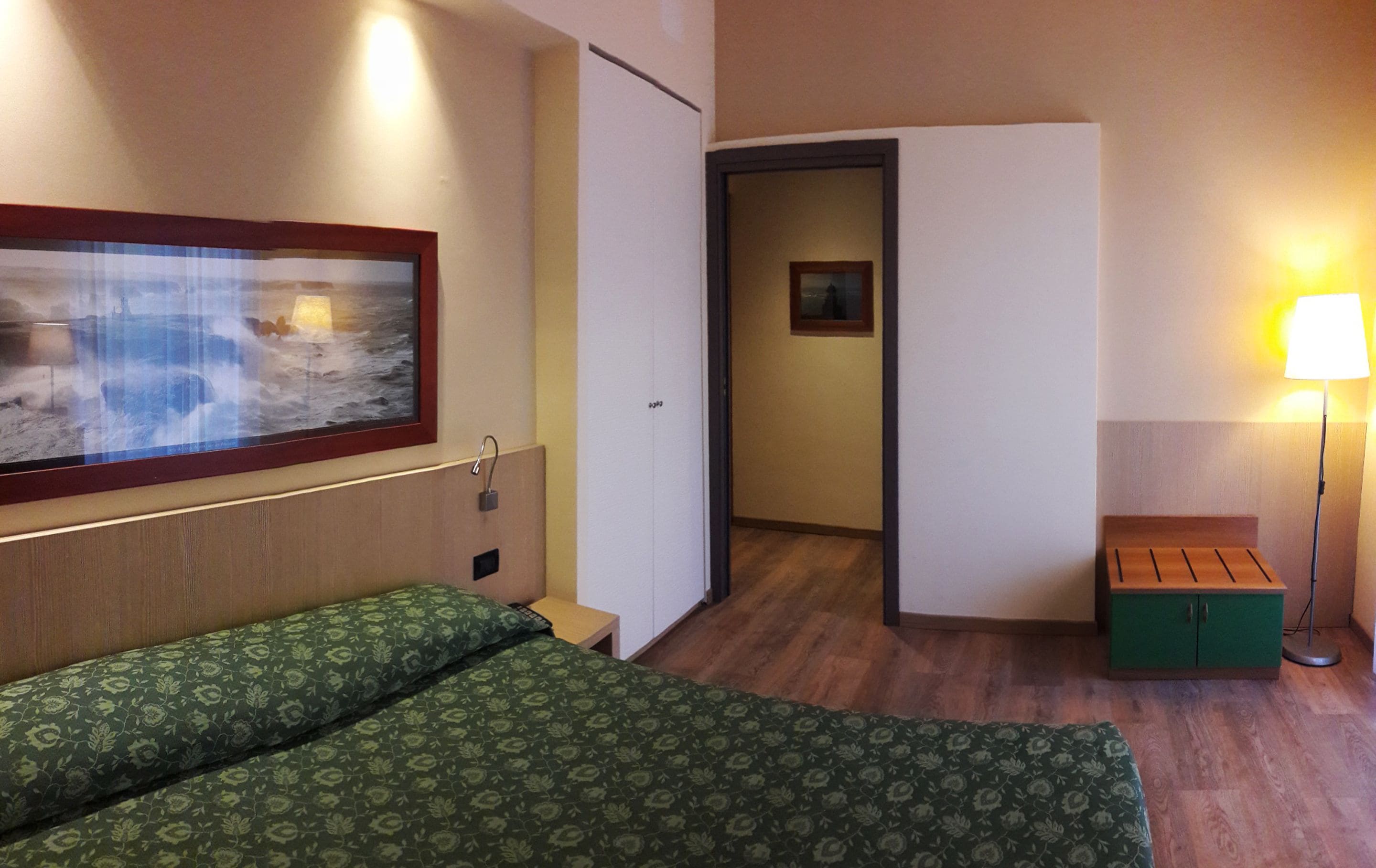Une chambre d’hôtel avec un lit, un tableau, un bureau et une lampe.