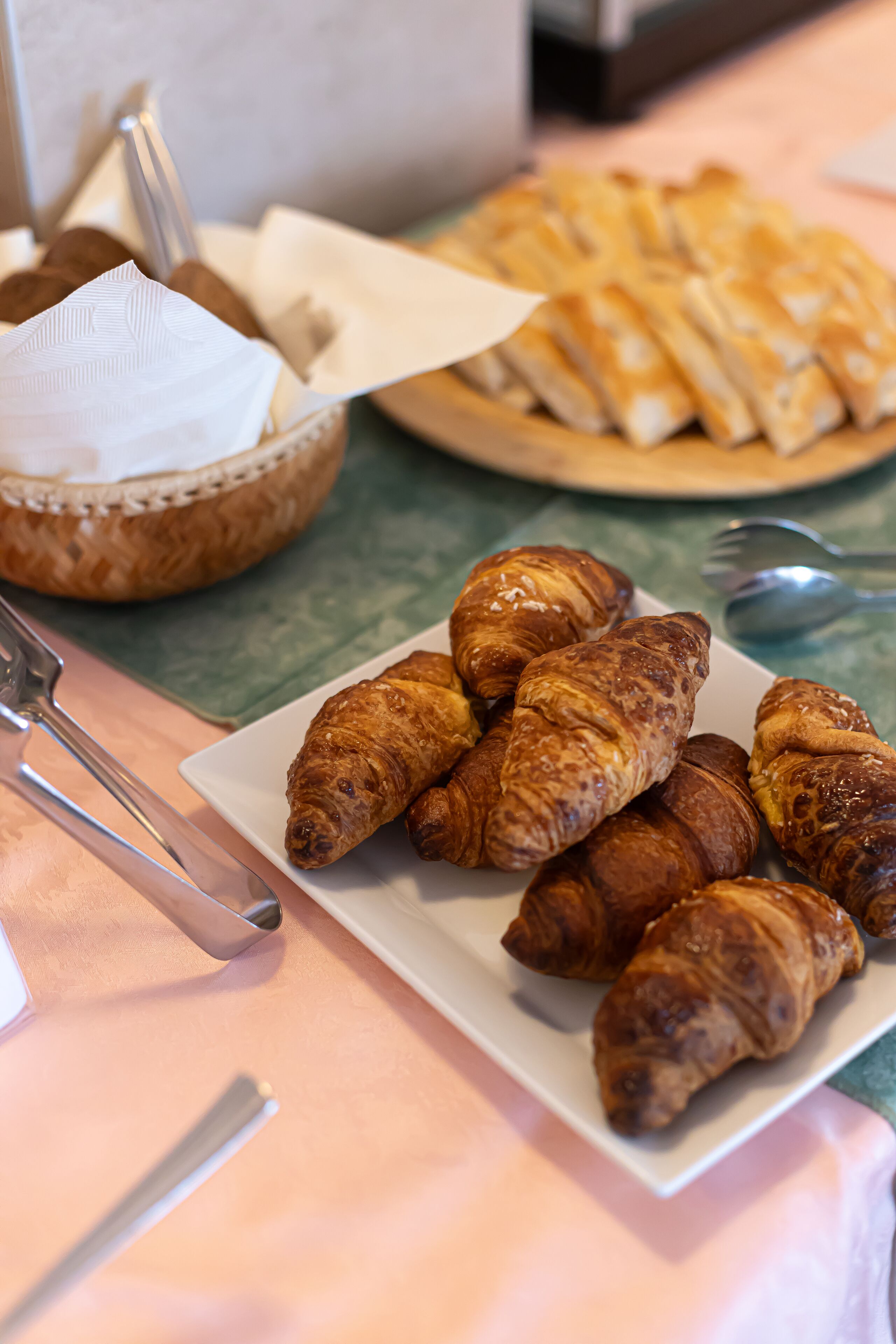 A plate of croissants and a basket of bread on a table.