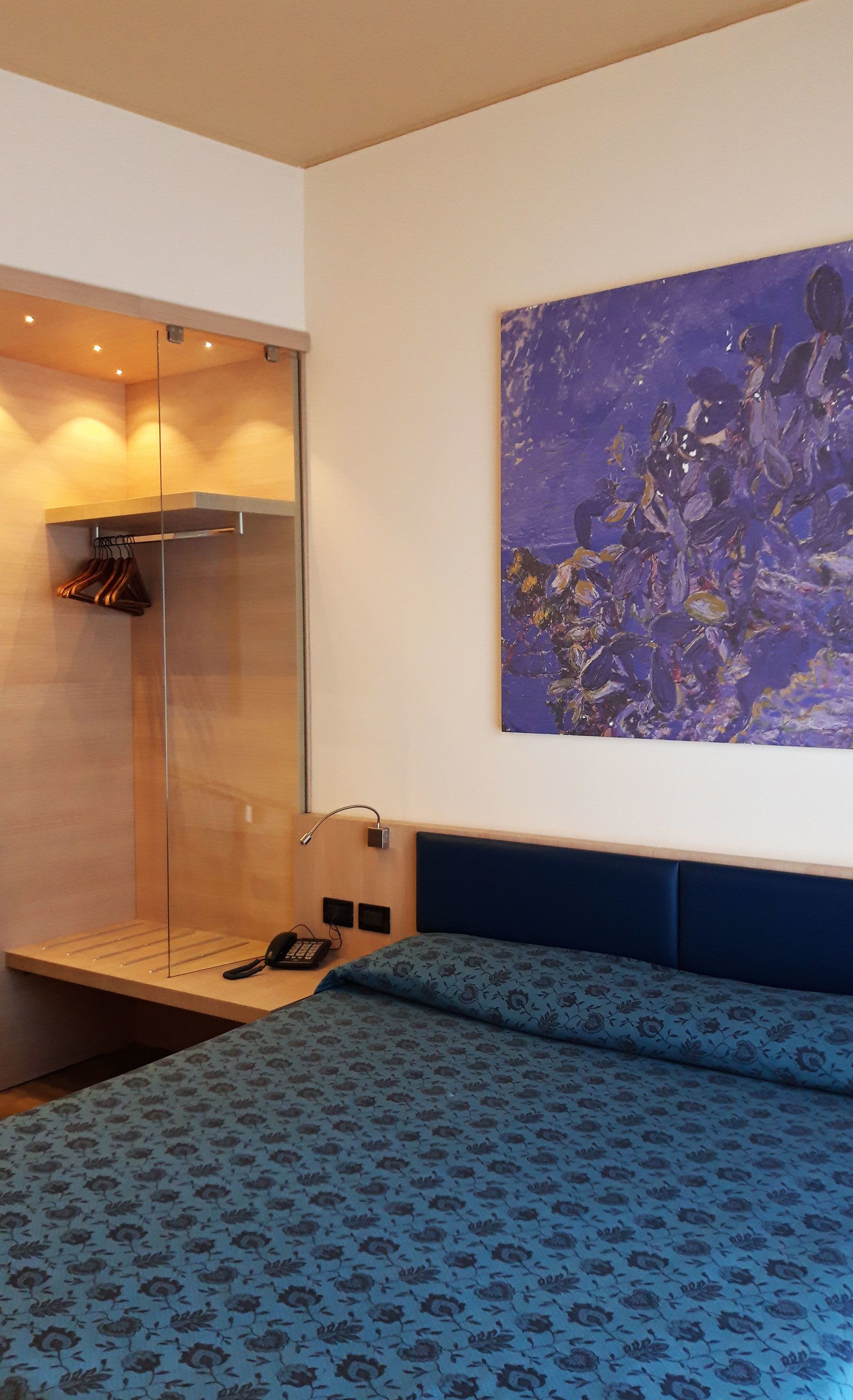 Moderni hotellihuone, jossa on sänky, suihkutila ja suuri, abstrakti taulu seinällä.