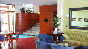 Uma sala de estar com escada de madeira, poltronas azuis, um sofá riscado e um espaço de jantar com mesa e cadeiras.