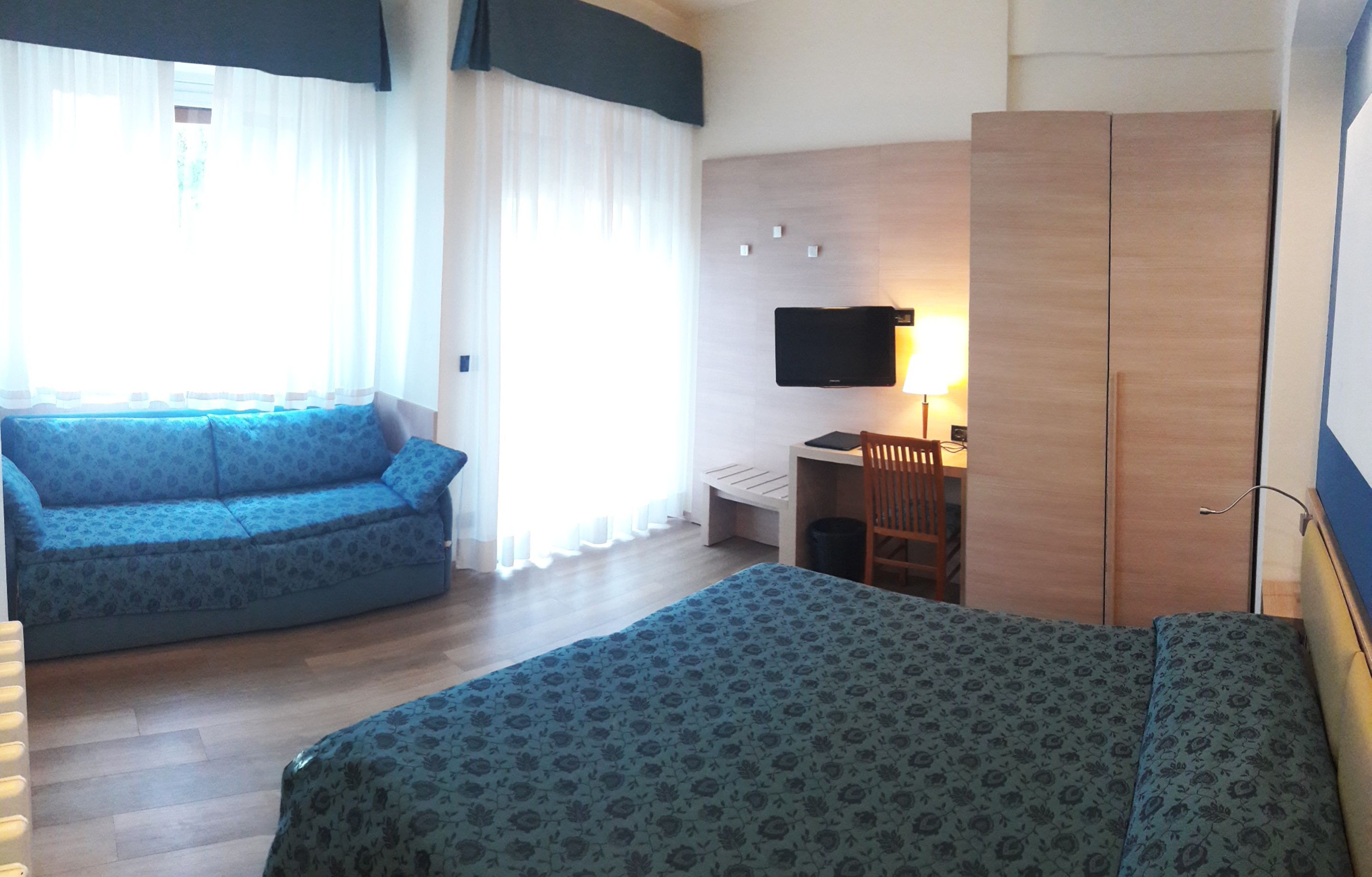 A hotel room with a bed, a sofa, a desk, and a TV.