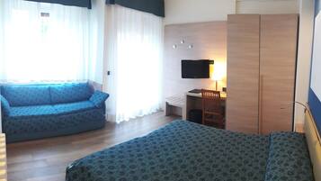 A hotel room with a bed, a sofa, a desk, and a TV.