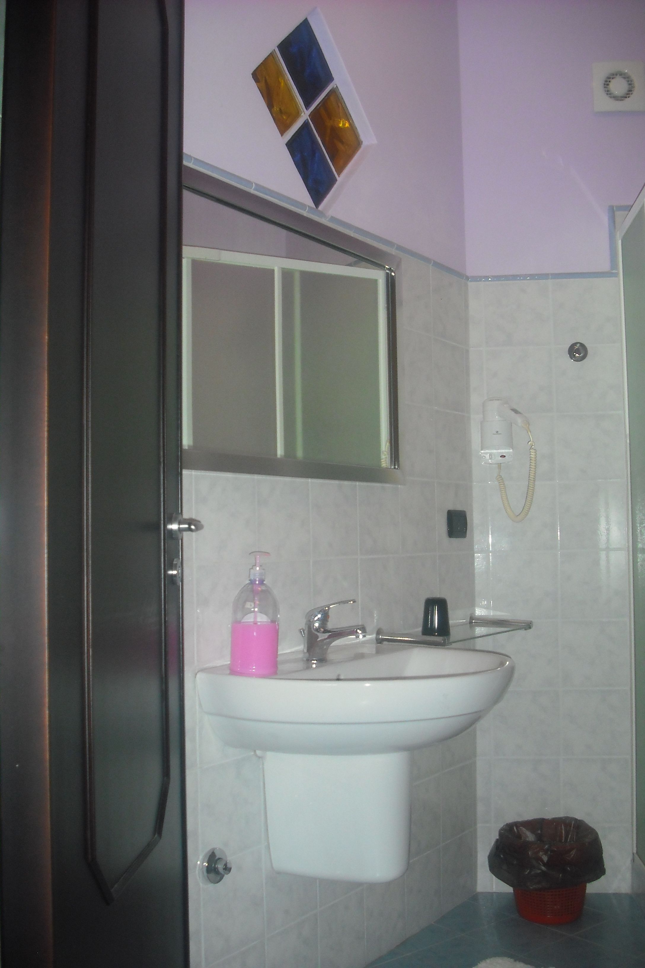 A bathroom with a white sink, a mirror, a hand dryer, and a trash bin.