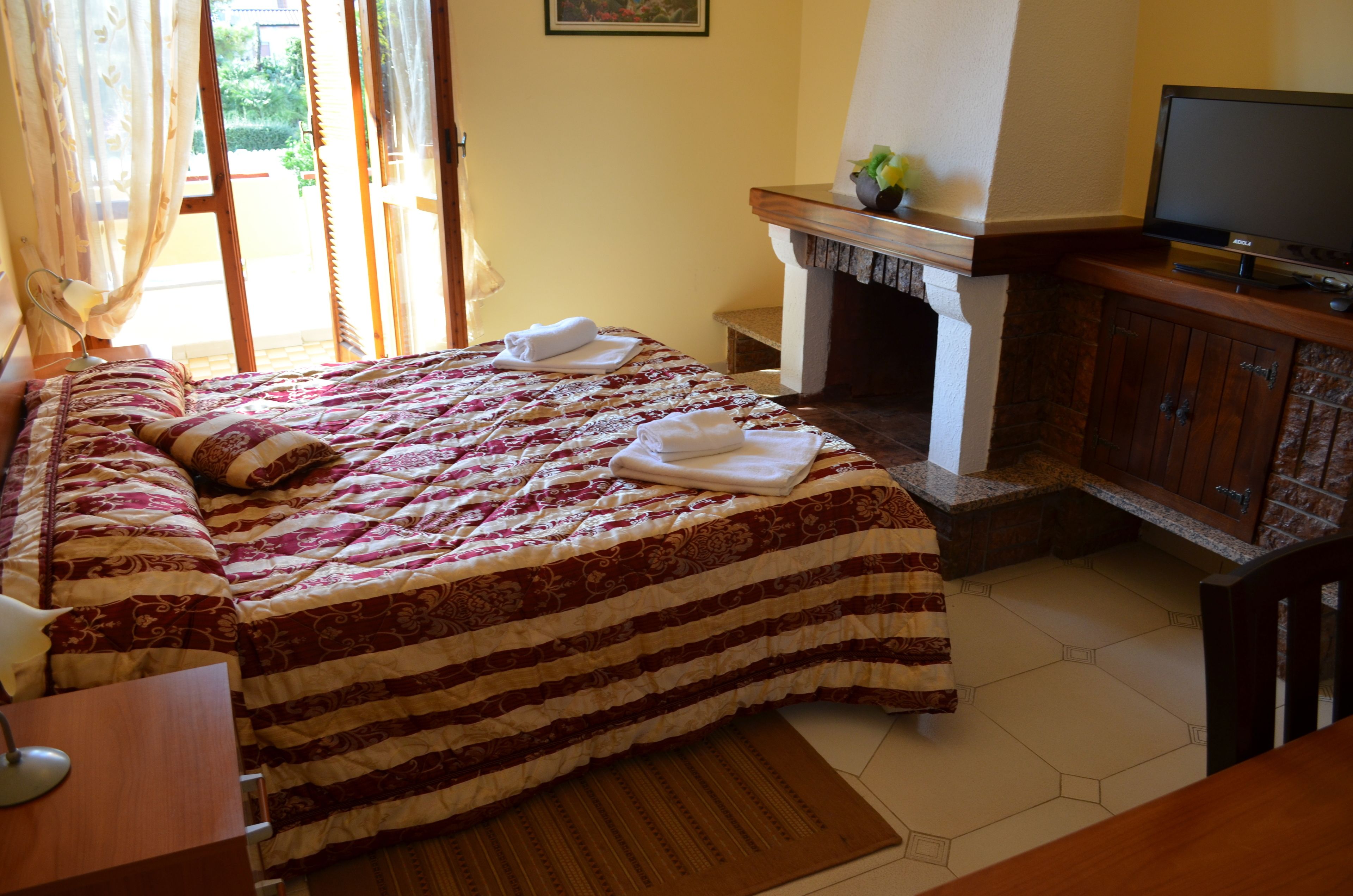 A bedroom with a large bed, a television, a fireplace, and a dining area.