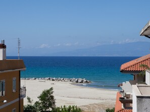 A coastal view with a sandy beach, rocky breakwater, and buildings with balconies overlooking the sea. - Barbieri (Vibo Valentia)