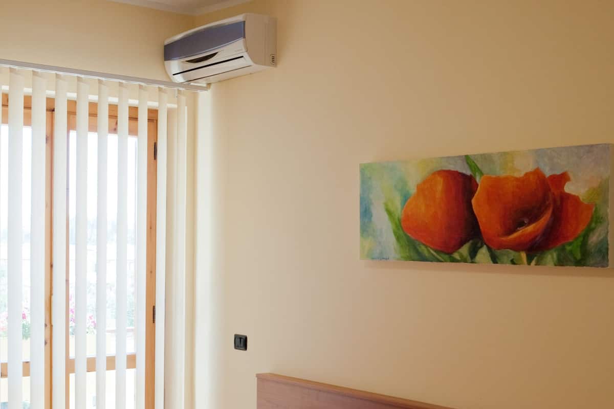 Una habitación de hotel con una cama, un cuadro de flores en la pared y un equipo de aire acondicionado.