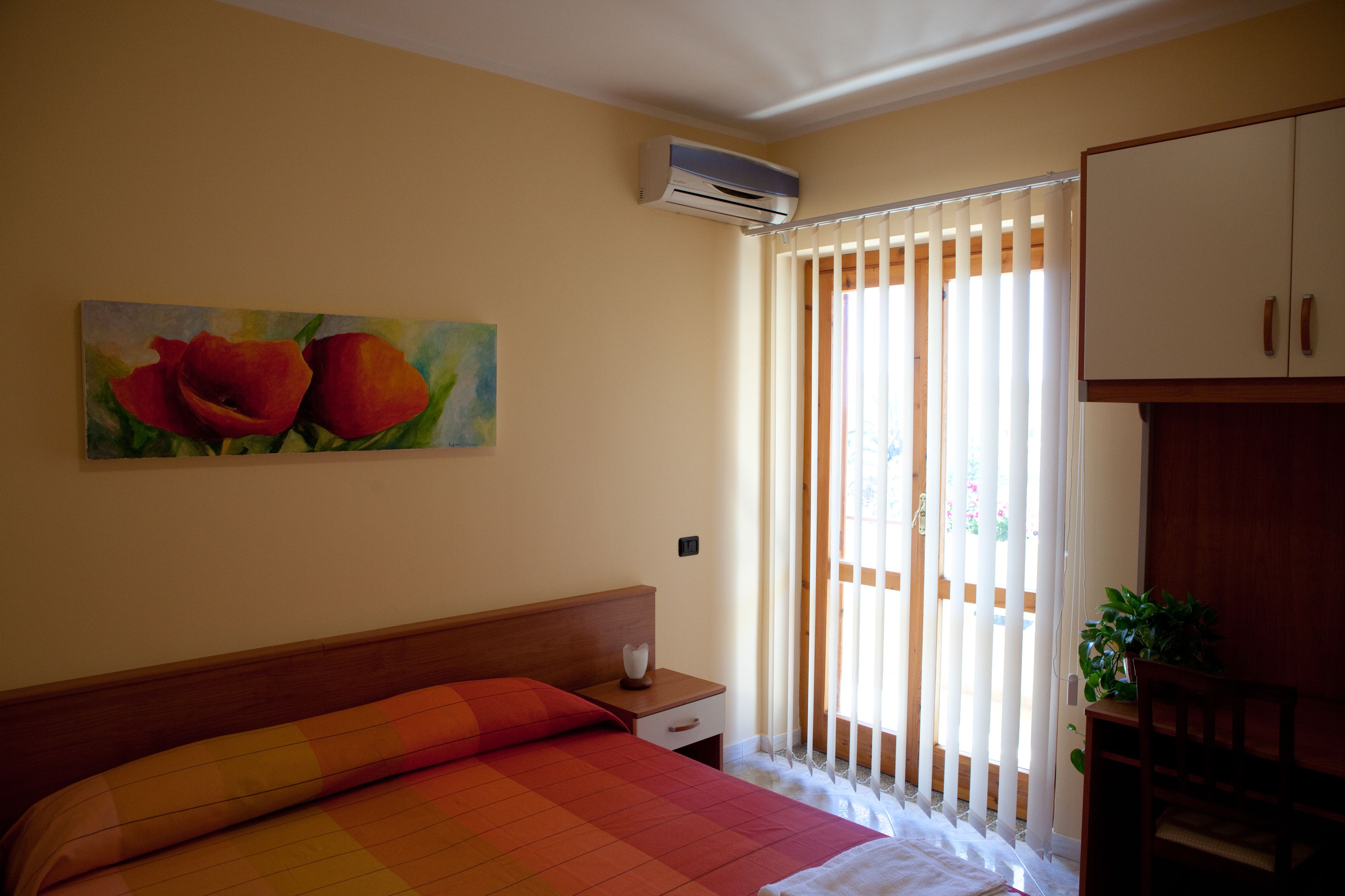 Camera da letto con un letto, un comodino, un condizionatore, un quadro di fiori e una porta scorrevole.