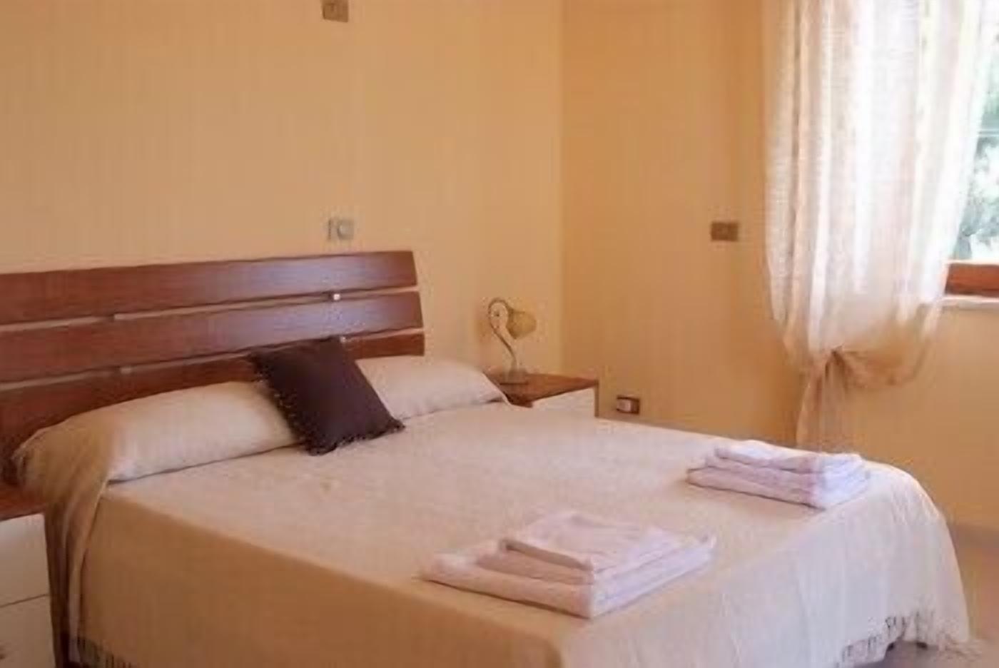 A neatly made bed with a wooden headboard, a bedside lamp, and a window with curtains.