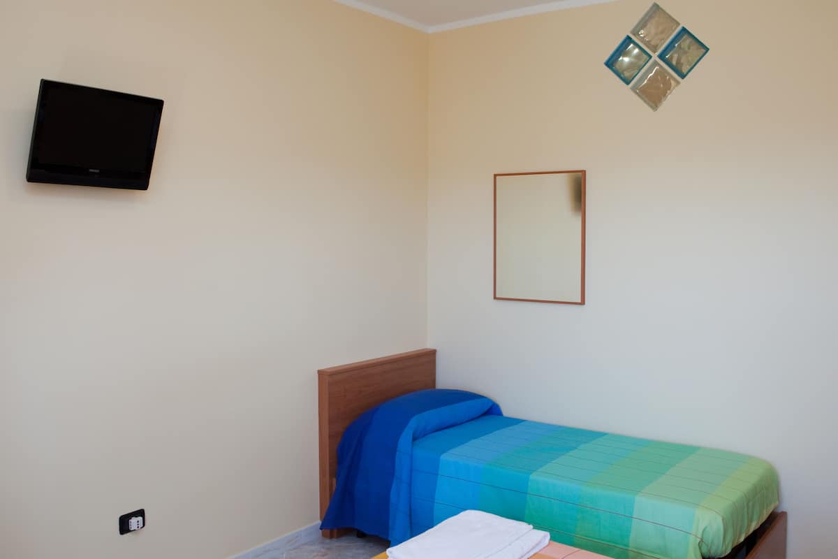 Un dormitorio con cama, televisor montado en la pared y un espejo pequeño.