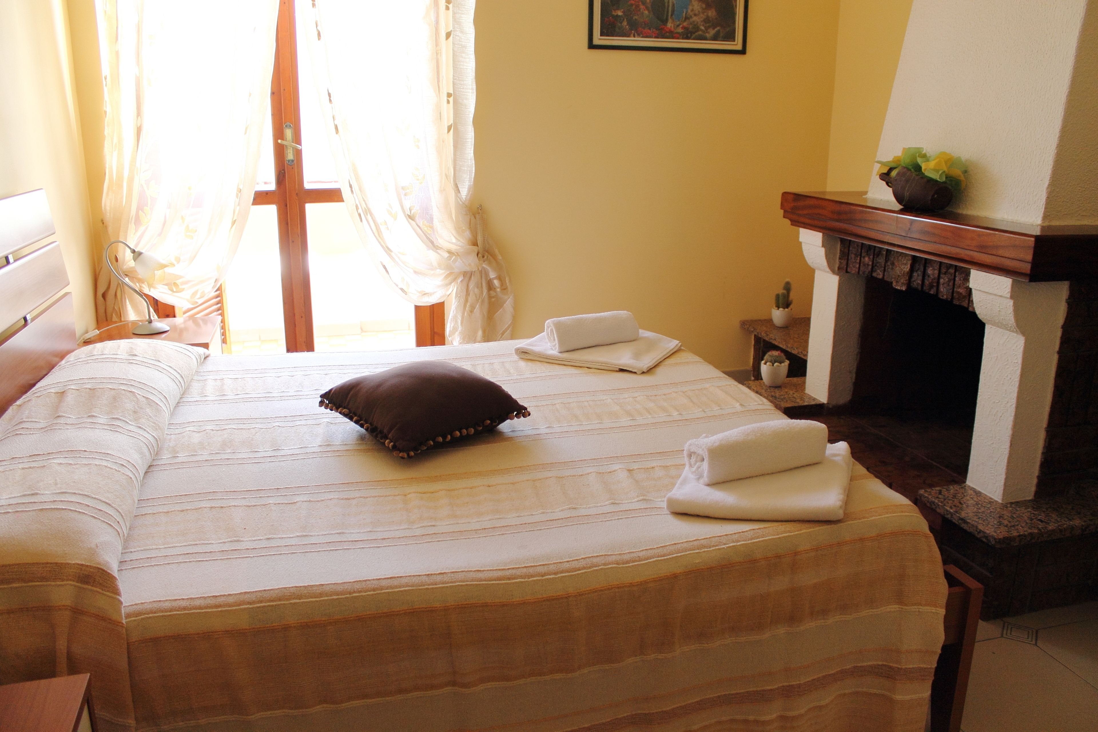A hotel room with a large bed, a wooden headboard, a fireplace, and a window with curtains.