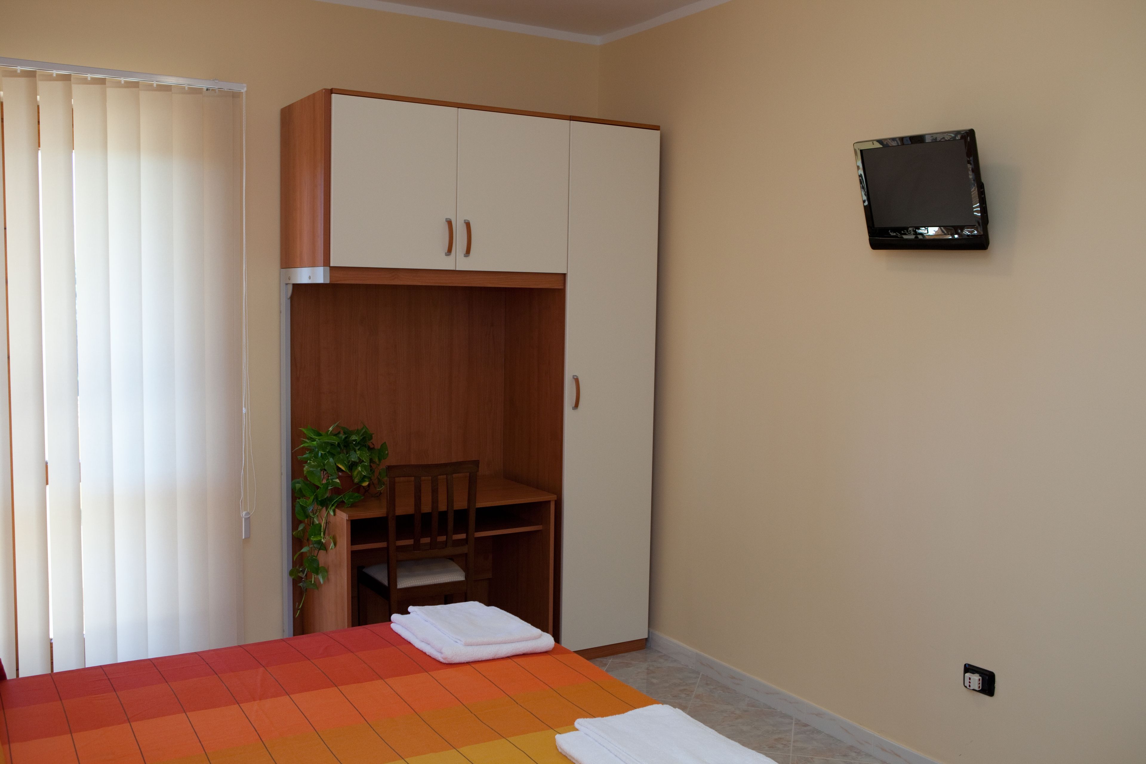 Una camera da letto con un letto, una scrivania, una sedia, una televisione e una finestra con tende.