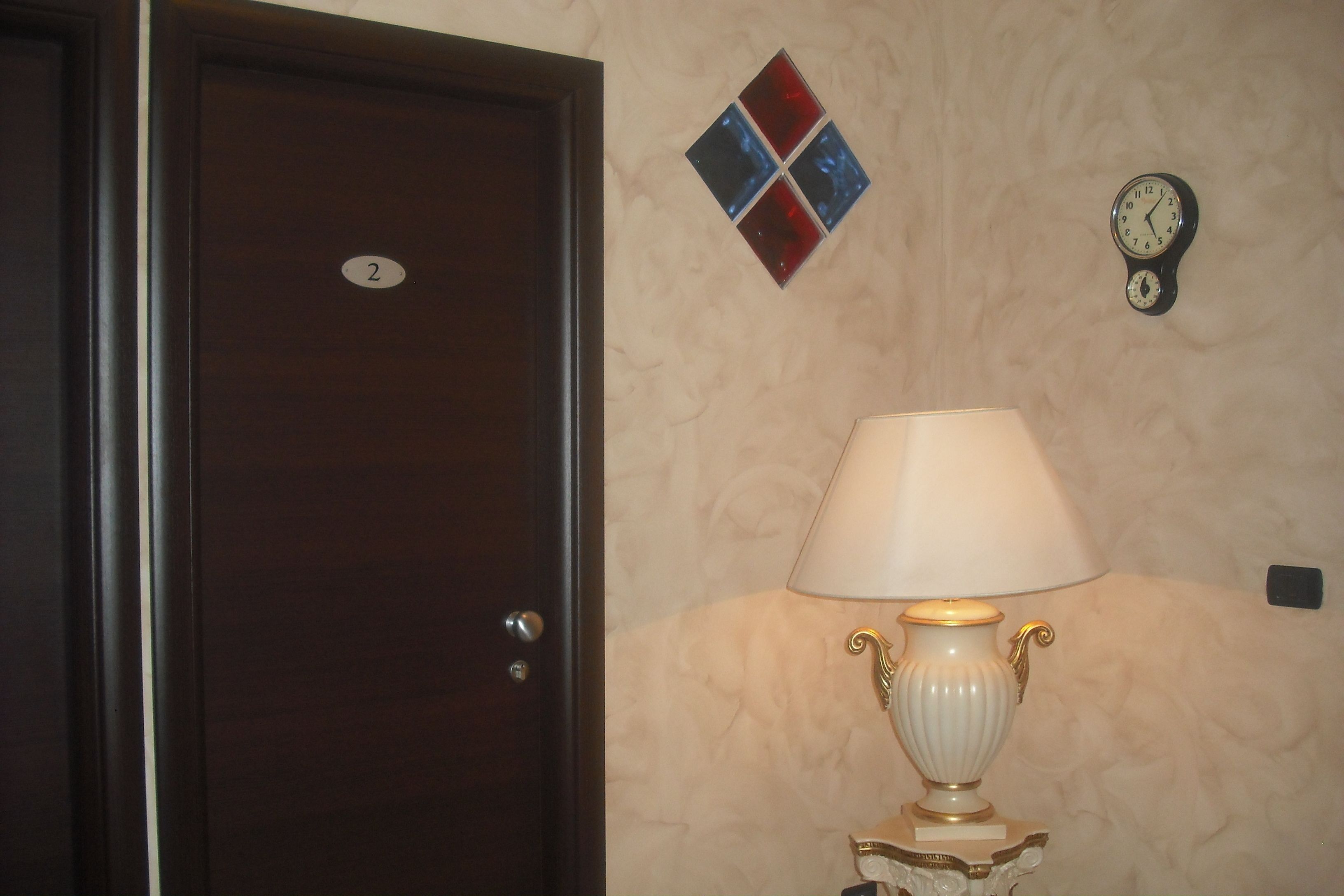 A room with a closed door, a wall clock, and a table lamp.