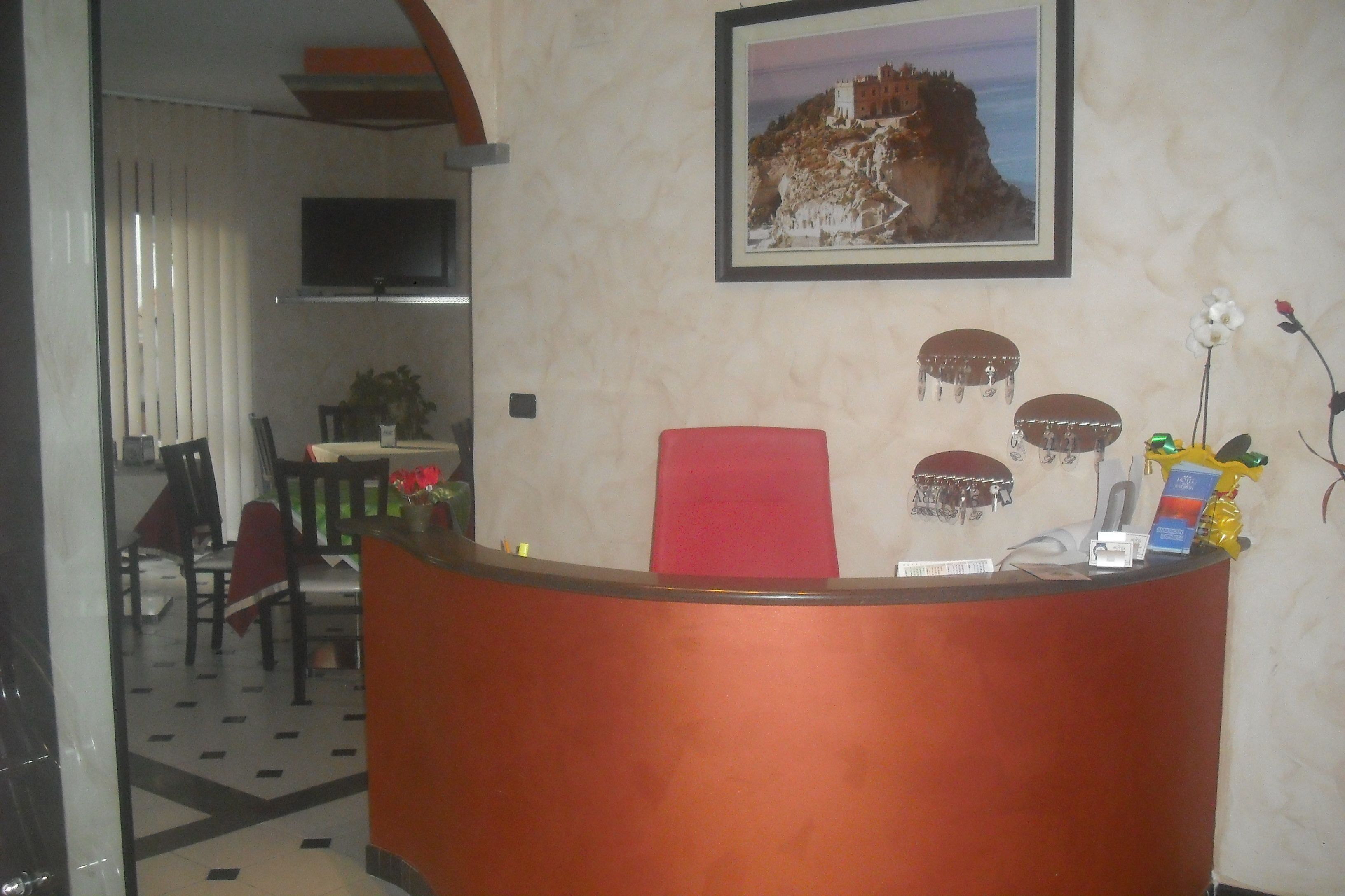A reception area with a red desk, a framed picture of a coastal building, and a small plant.