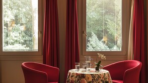 A room with two red chairs, a table with a floral tablecloth, and two windows with red curtains. - Albergo Al Moretto (Castelfranco Veneto)