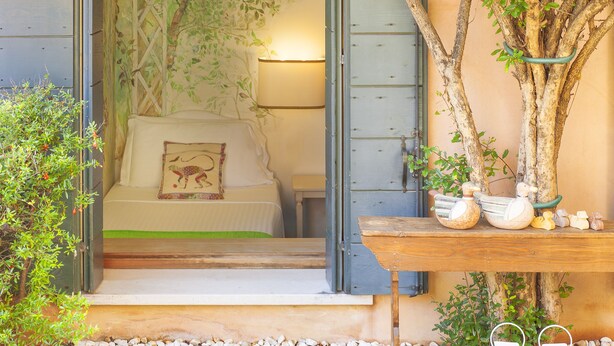 A cozy room with a bed, a wall mural, a lamp, and a wooden shelf with decorative items. - Albergo Al Moretto (Castelfranco Veneto)