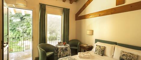 A hotel room with a bed, two chairs, a small table, and a window with curtains.