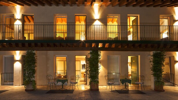 Un hotel con una zona de estar exterior cubierta, varios balcones y plantas en macetas.