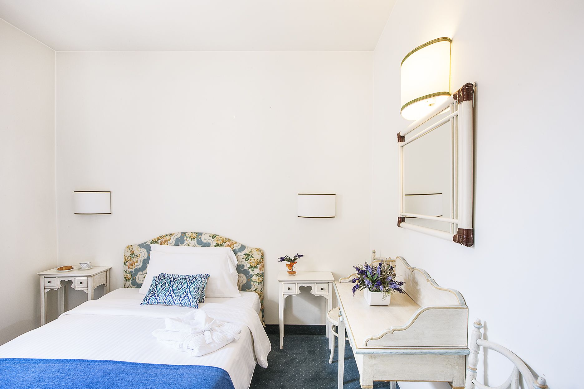A hotel room with a bed, bedside tables, a dresser, a mirror, and wall-mounted lamps.