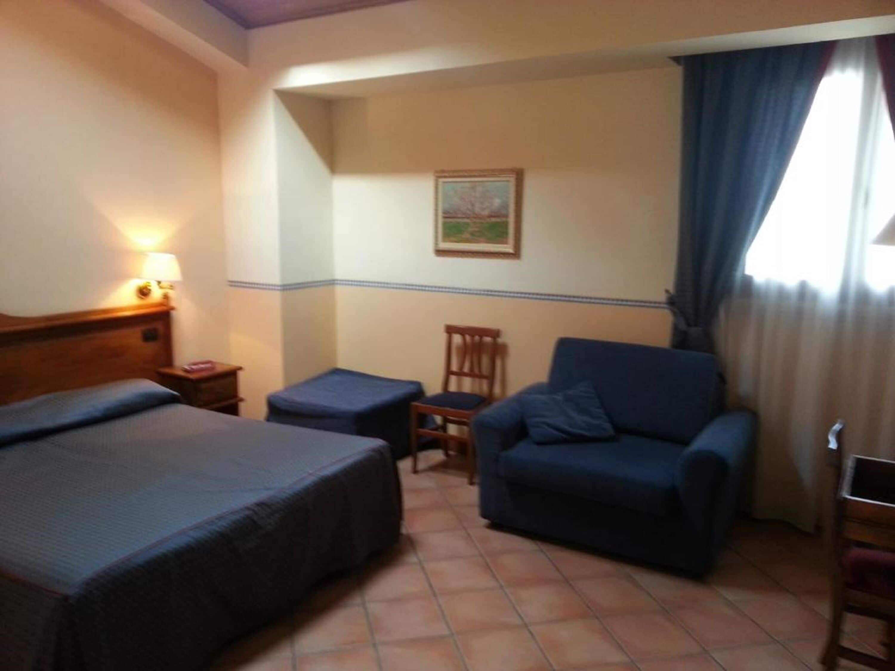 Een hotelkamer met twee bedden, een stoel, een tafeltje en een schilderij aan de muur.