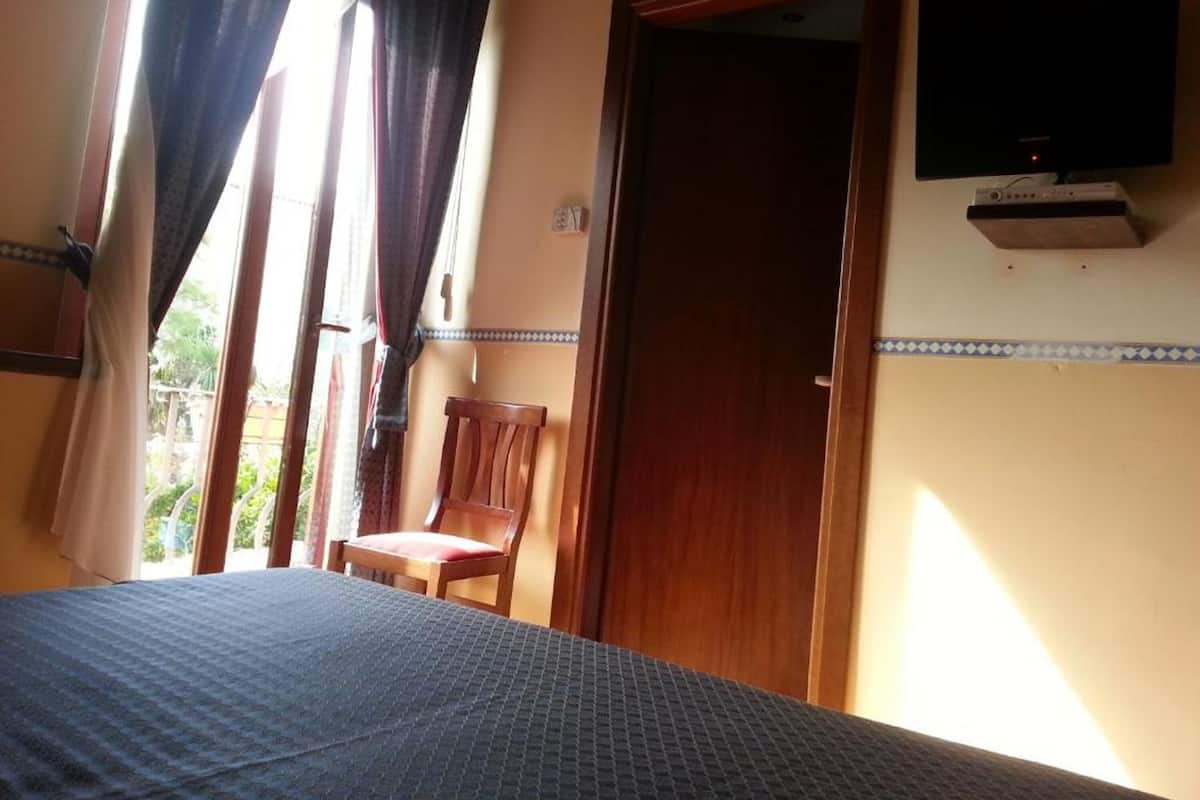 A bedroom with a bed, a chair, a television, and a door.