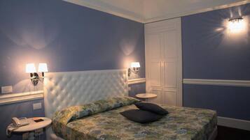 Une chambre à coucher avec une tête de lit capitonnée, une couvre-lit à motifs floraux, deux lampes de chevet, un téléphone sur la table de chevet et une table ronde.