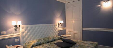 Un dormitorio con cabecera capitonada, edredón estampado con flores, dos lámparas de noche, teléfono junto a la cama y una mesa redonda.