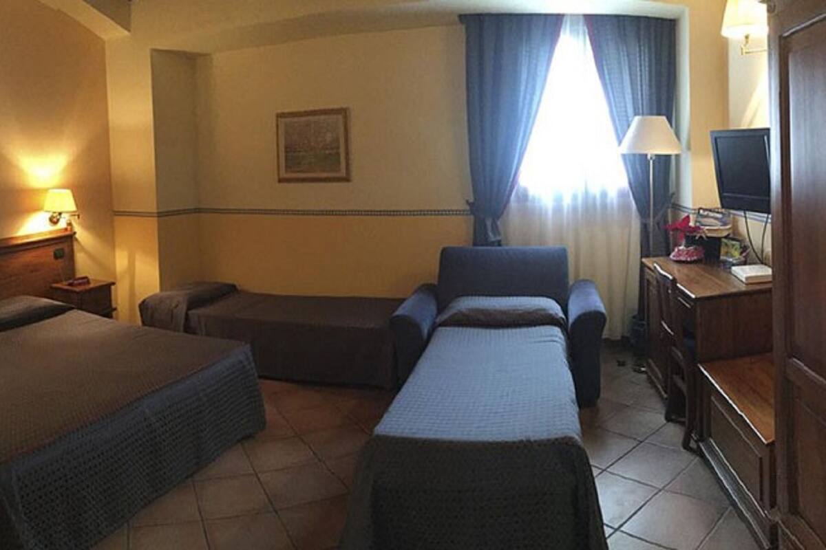 A hotel room with two beds, a desk, a chair, a television, and a window with curtains.