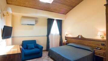 A hotel room with a wooden ceiling, a bed with a headboard, a blue sofa, a desk with a lamp, and a television.