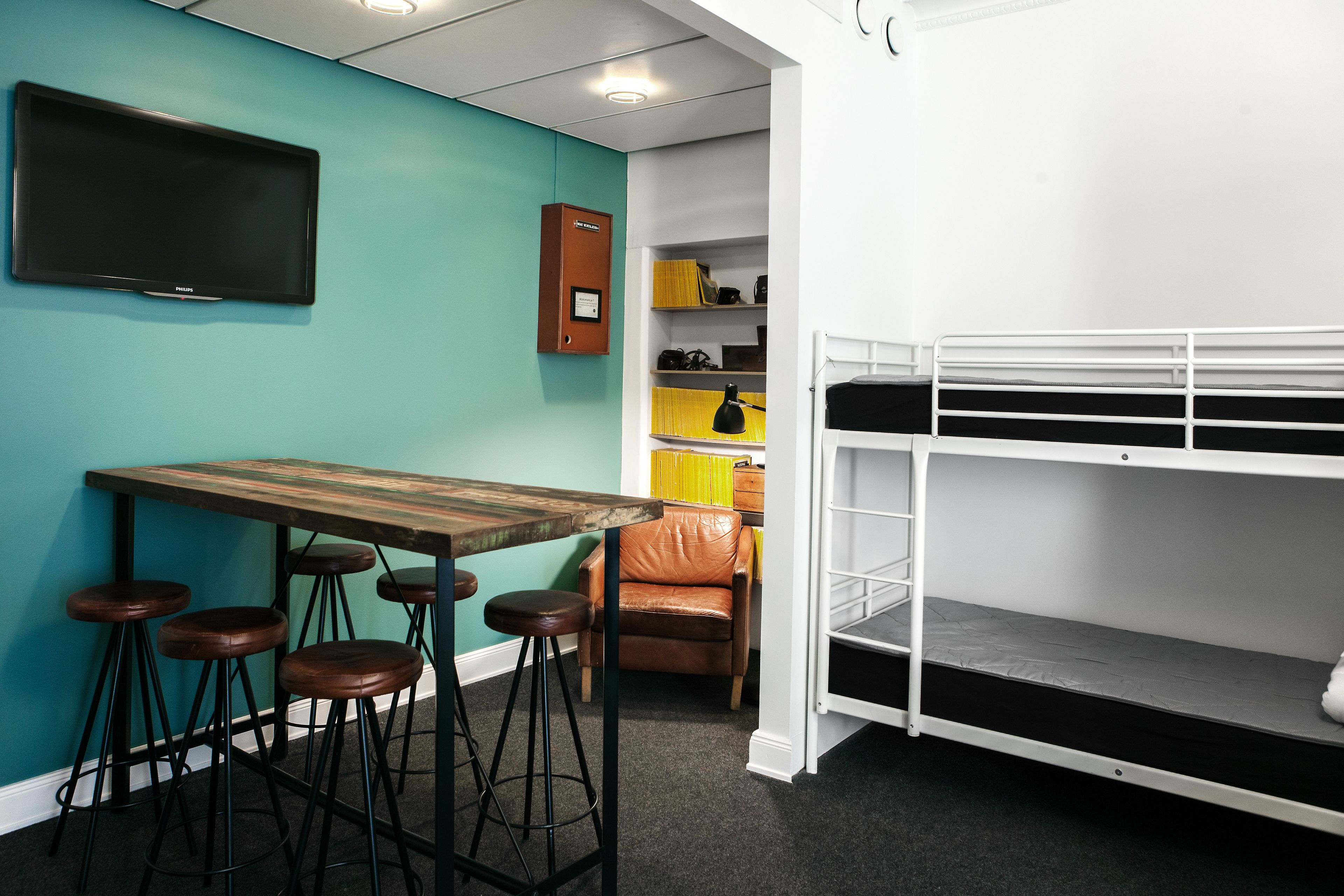 A bunk bed, a table with stools, a TV, and a cabinet in a room with teal walls.