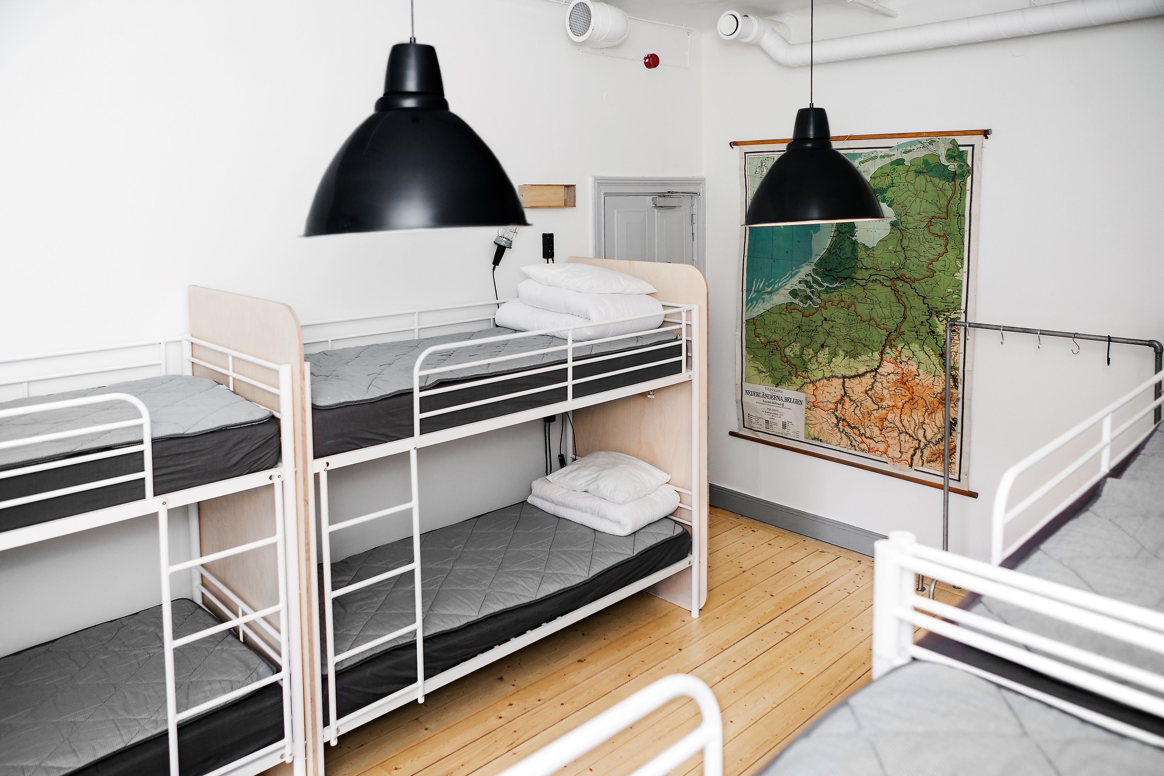 A bunk bed room with a map on the wall, a white door, and a black pendant light.