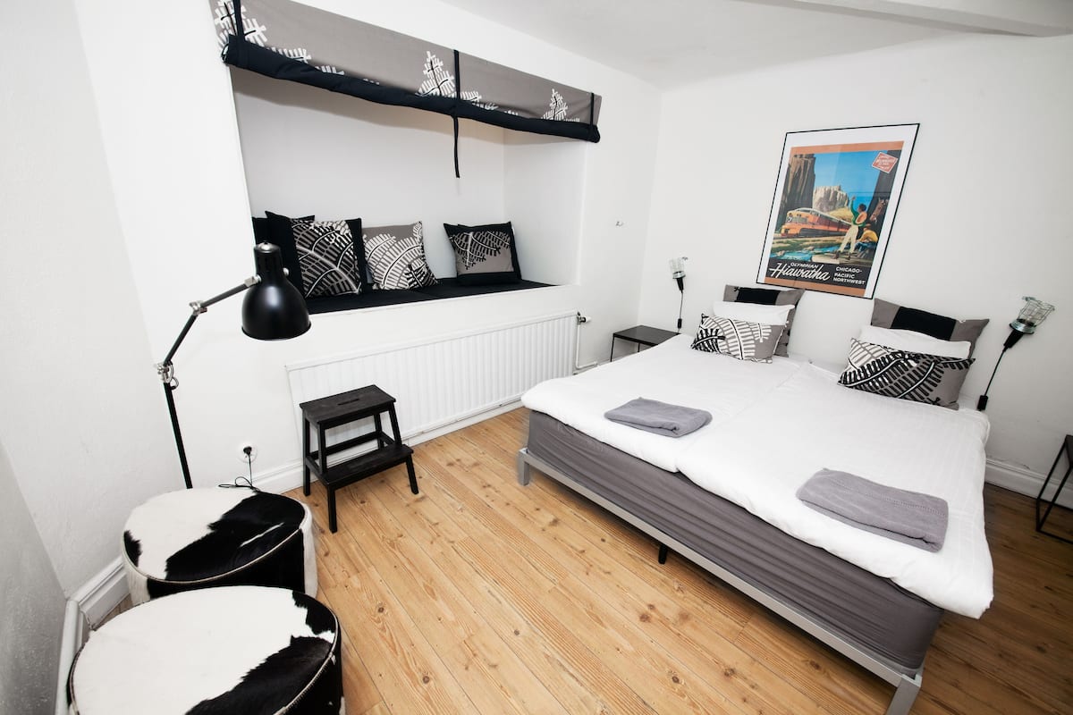 A bedroom with a bed, bedside tables, a radiator, a hanging shelf, and a poster on the wall.