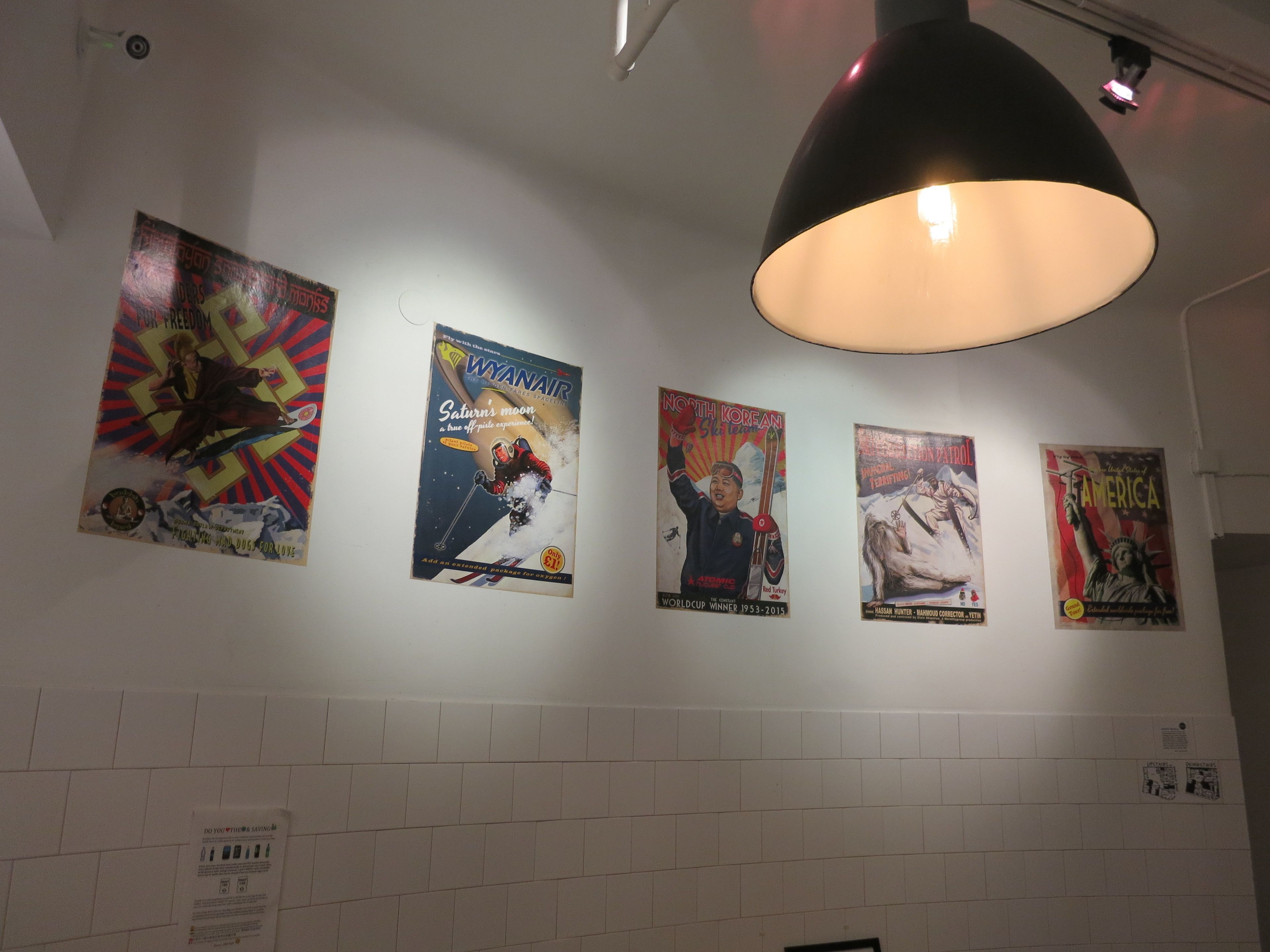 A wall with four posters, a light fixture, and a tiled wall.