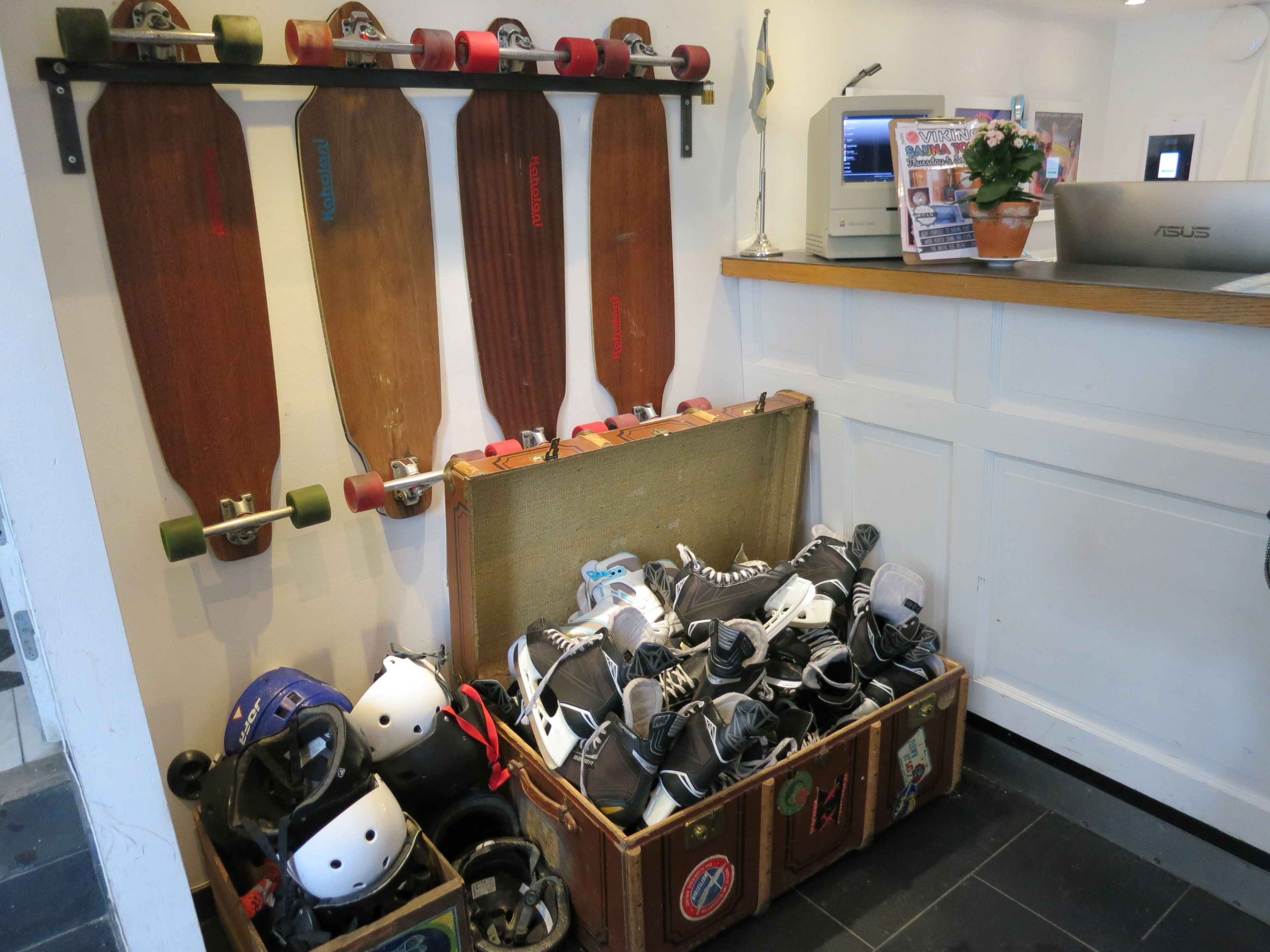 A storage area with a wooden case filled with helmets and shoes, a wall-mounted rack with paddles, and a computer on a desk.