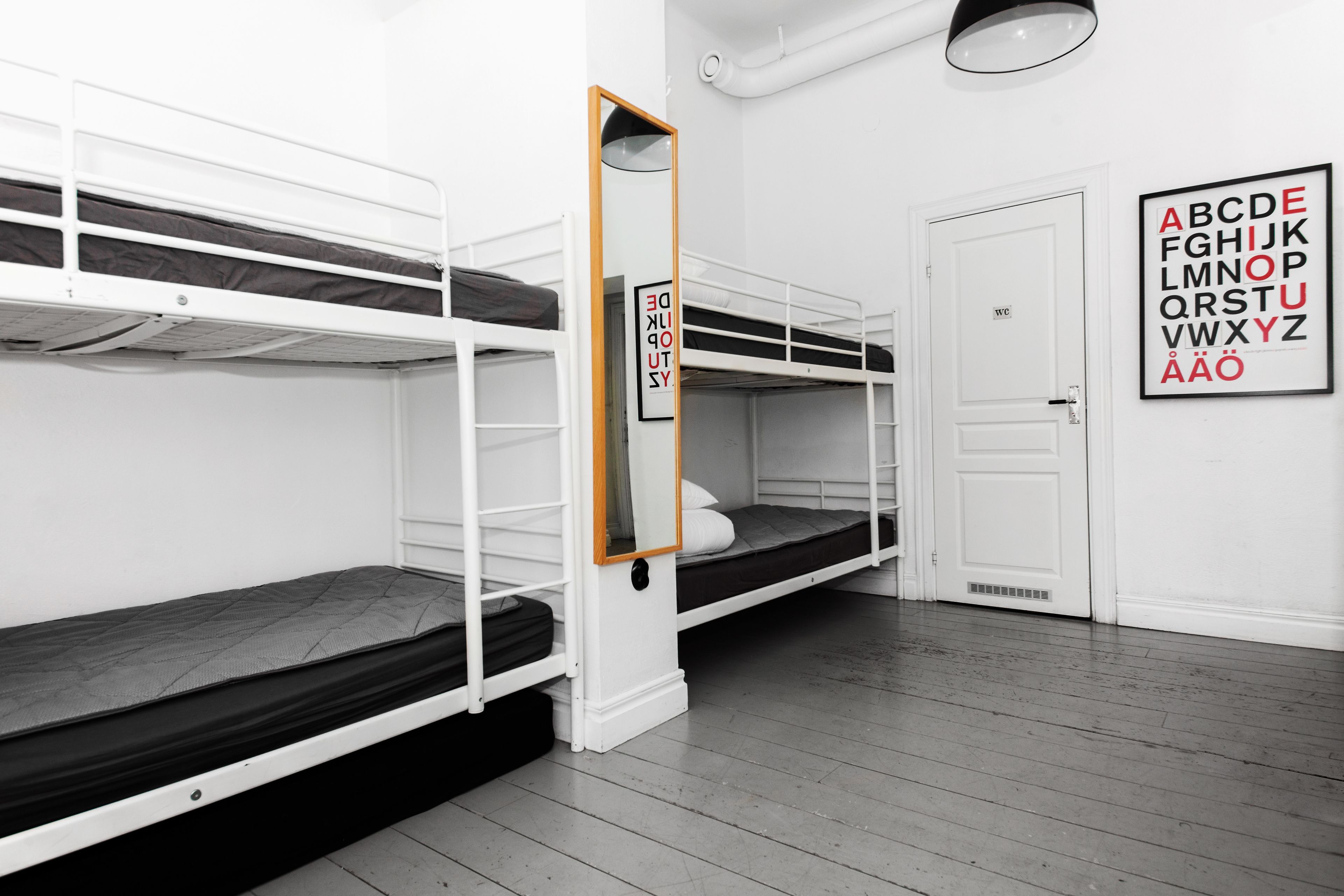 Um quarto em dormitório com beliches, um espelho, um cartaz com o alfabeto emoldurado e uma porta branca.