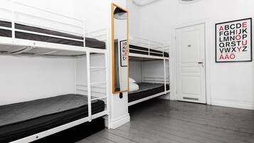 Um quarto em dormitório com beliches, um espelho, um cartaz com o alfabeto emoldurado e uma porta branca.