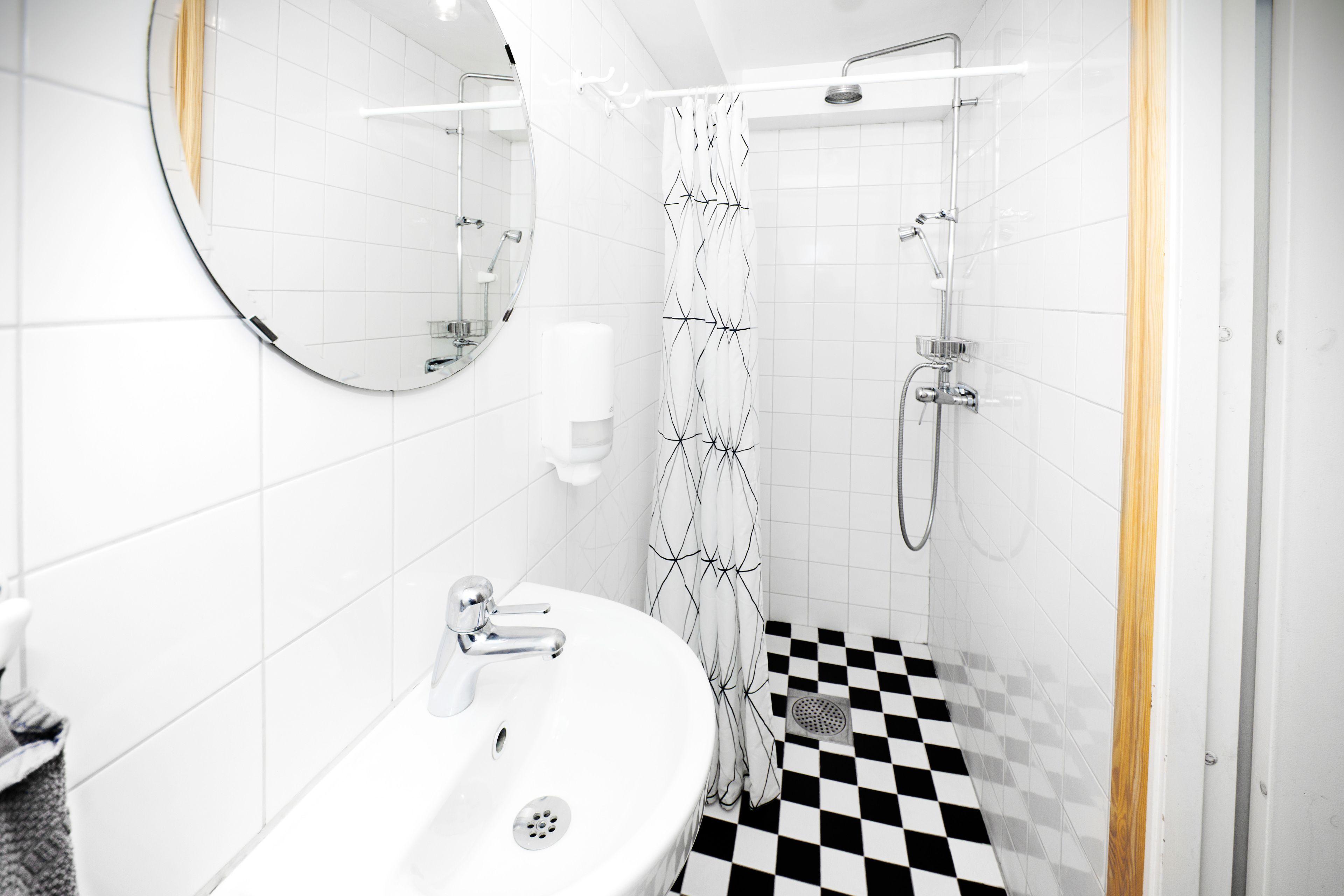 A modern bathroom with a white sink, a mirror, a shower with a black and white checkered floor, and a patterned shower curtain.