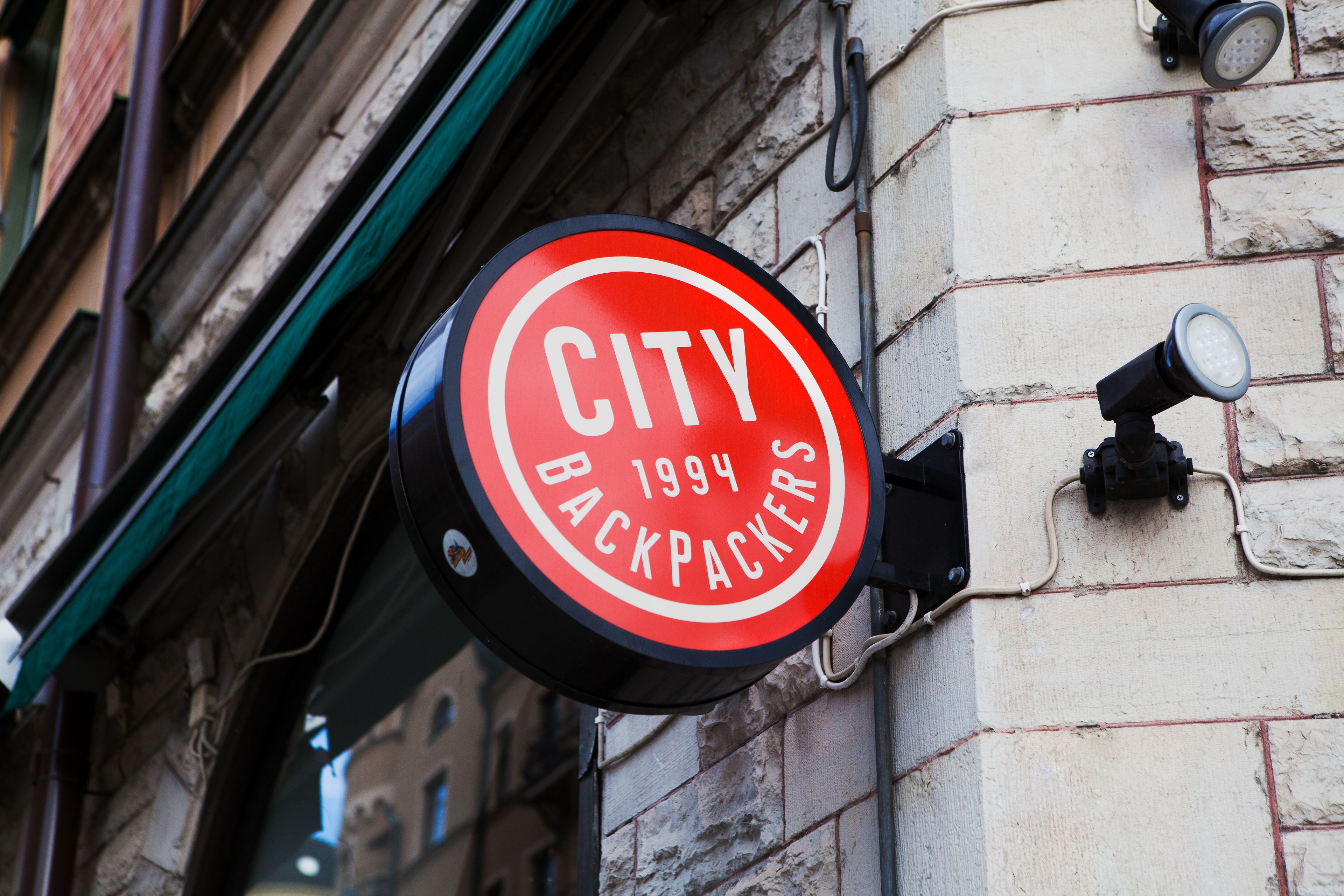 Ein rundes Schild mit dem Aufdruck "CITY BACKPACKERS 1994", das an einem Gebäude befestigt ist.