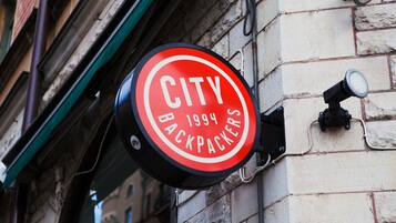 Ein rundes Schild mit dem Aufdruck "CITY BACKPACKERS 1994", das an einem Gebäude befestigt ist.