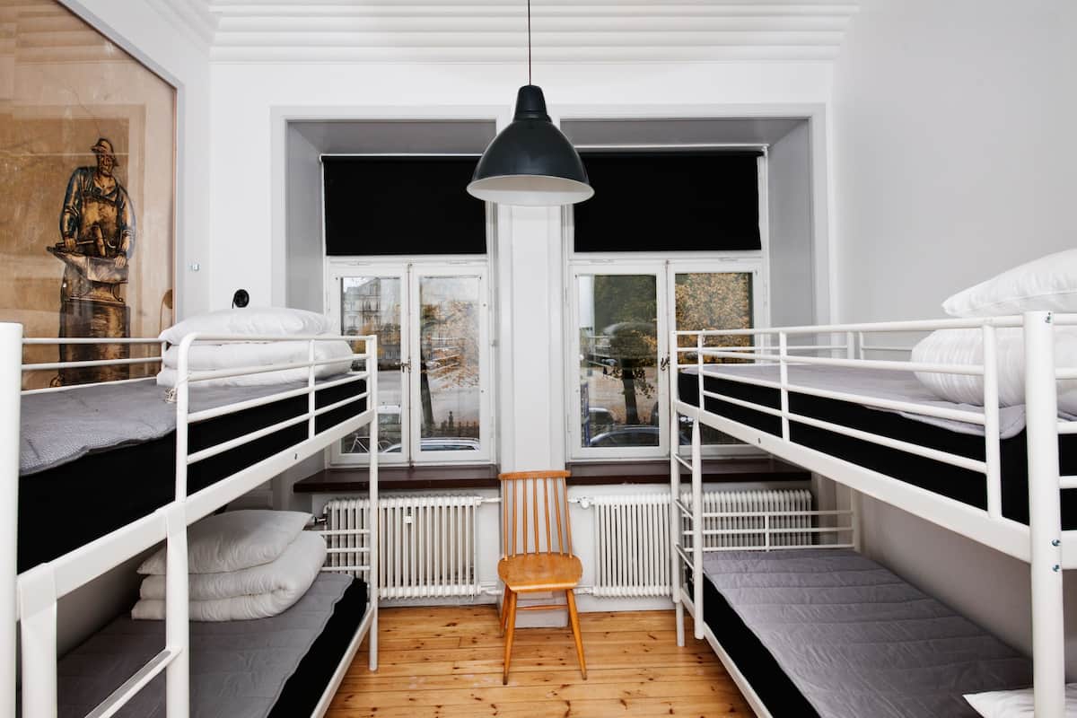 A dormitory room with bunk beds, a wooden chair, and a large window.