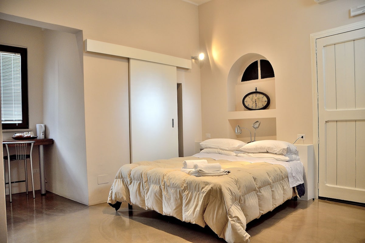 A bedroom with a bed, a bedside table, a clock, and a wardrobe.