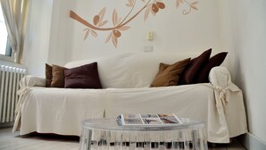 A living room with a white sofa, brown cushions, a clear glass coffee table, and a wall with a floral design. - Azzurretta (Lecce)