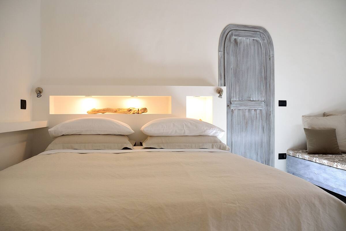 A bedroom with a bed, two bedside tables, a wardrobe, and wall-mounted lighting.