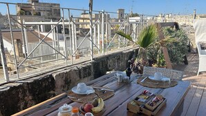 A wooden table set outdoors with breakfast items, including a bowl of fruit, a coffee pot, and jars of spreads. - Azzurretta (Lecce)