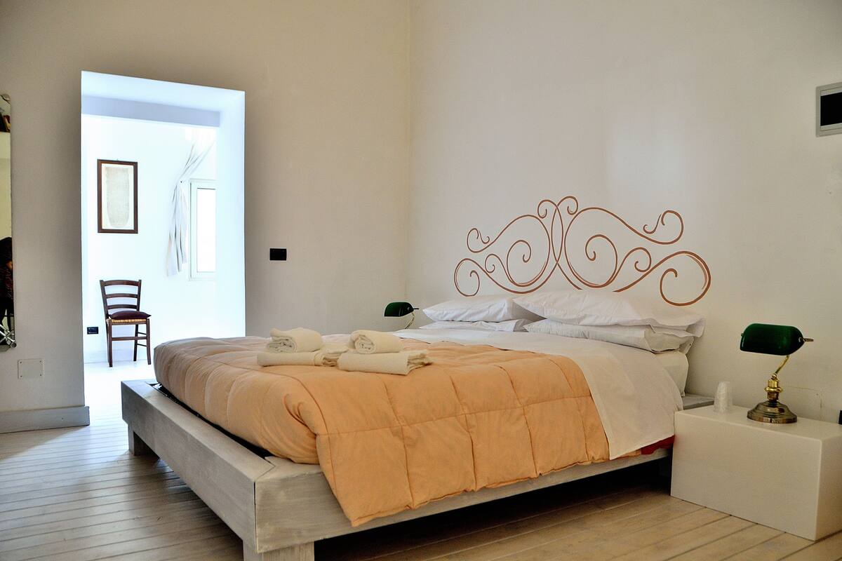 A bedroom with a bed, a nightstand, a chair, and a door leading to another room.